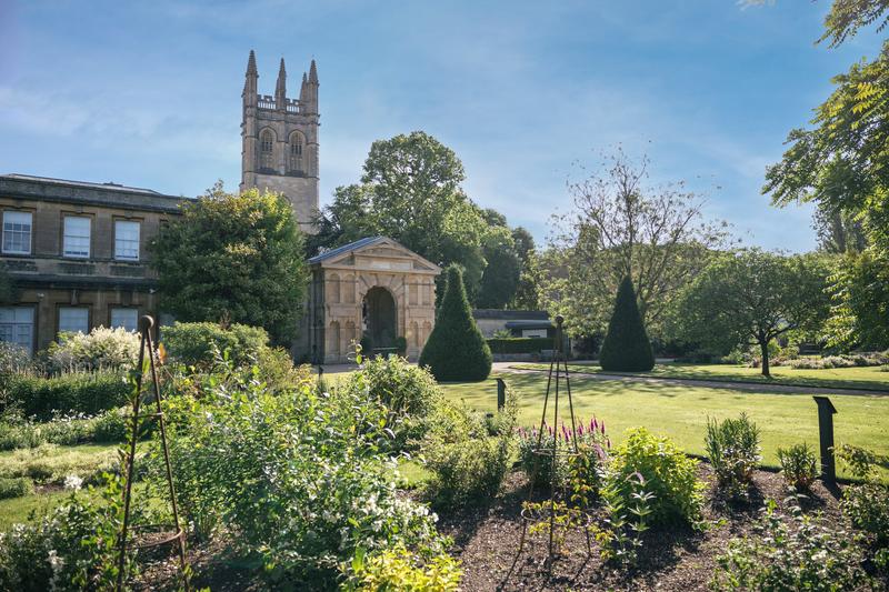 Oxford Botanic Gardens. Green garden with a large, stone building in the background.