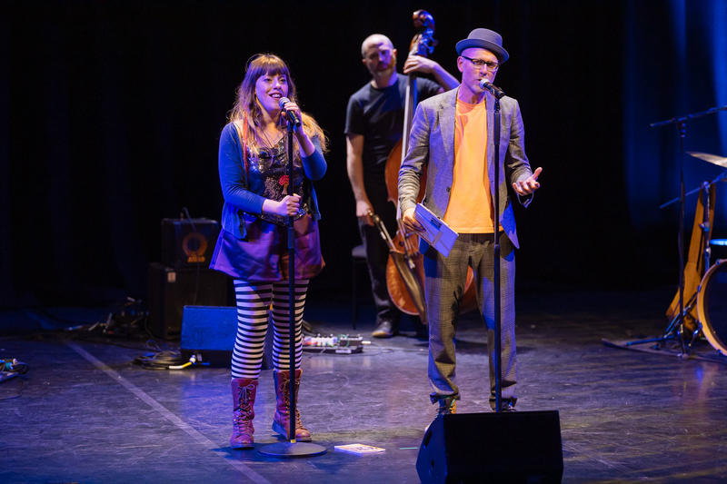 Two people standing on a dark stage in front of microphones