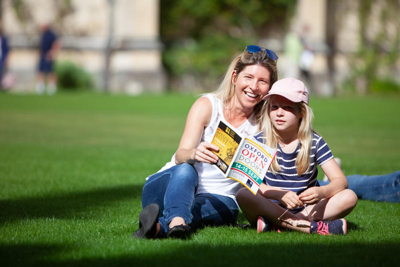 Mum and daughter sat in an open green space with an open doors leaflet