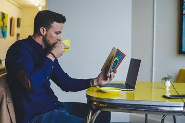 Male student drinking tea and reading a book at home 