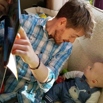 Ben holding a story book and pointing to it while reading to a small baby